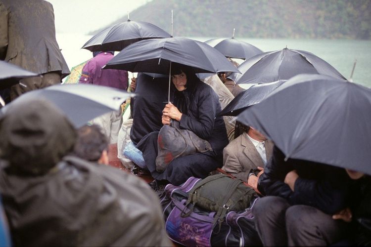 Menschen auf Boot unter Regenschirmen mit Gepäck, Foto