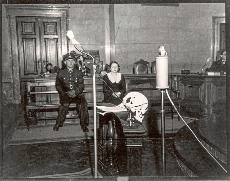 Der Schädel des mit einem Fleischwolf erschlagenen Johann Arthold mit Drähten und Schrauben zusammengehalten im Gerichtssaal. Im Hintergrund die Täterin auf der Anklagebank.