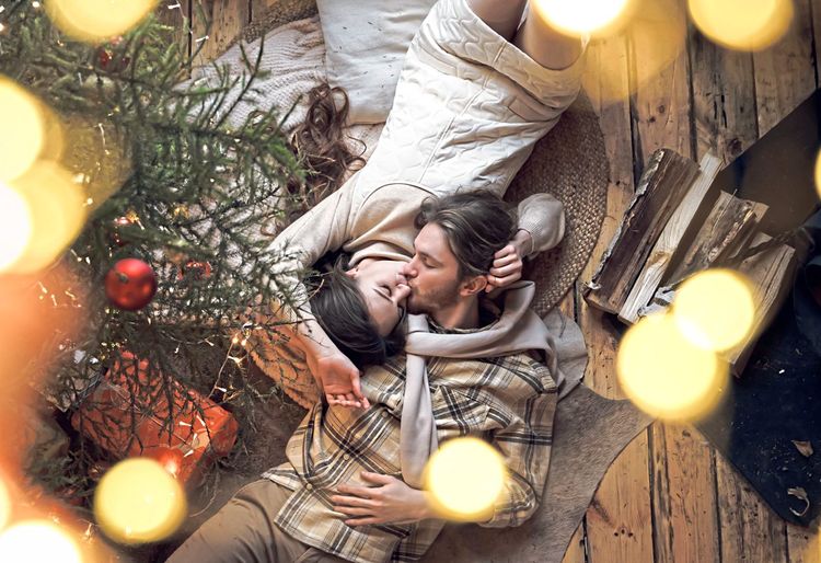 Junges Paar liegt unterm Christbaum und küsst sich