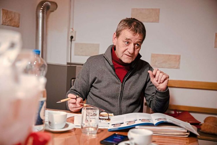 Erwin Kasper sitzt mit einem Stift in der Hand an einem Tisch, auf dem verschiedene Dokumente ausgebreitet liegen