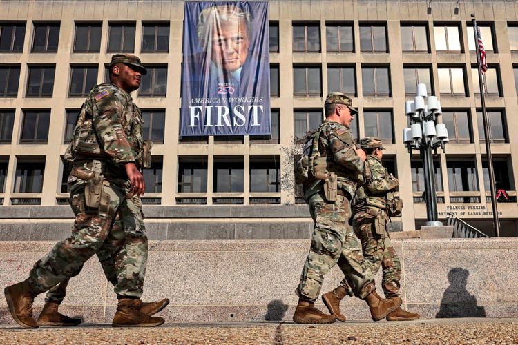 Mitglieder der Nationalgarde gehen vor dem Gebäude des US-Arbeitsministeriums in Washington, D.C., vorbei. Im Hintergrund ist ein großes Banner mit der Aufschrift „AMERICAN WORKERS FIRST“ und einem abgebildeten Gesicht zu sehen.