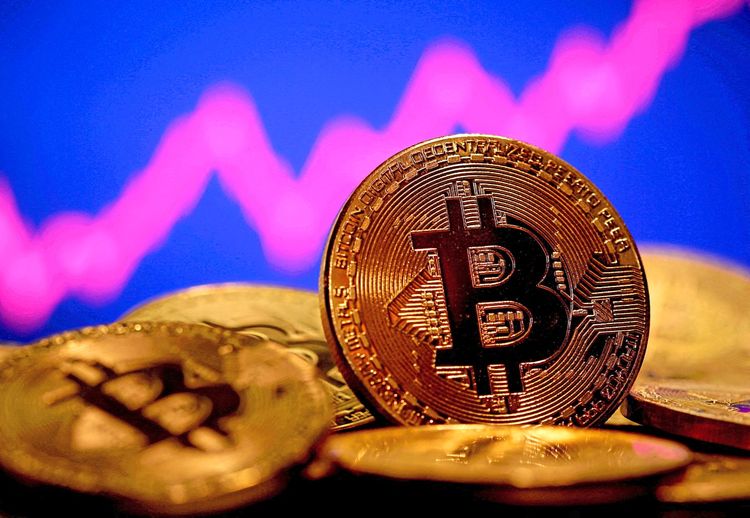 Eine Darstellung der virtuellen Währung Bitcoin ist vor einer Aktiengrafik zu sehen