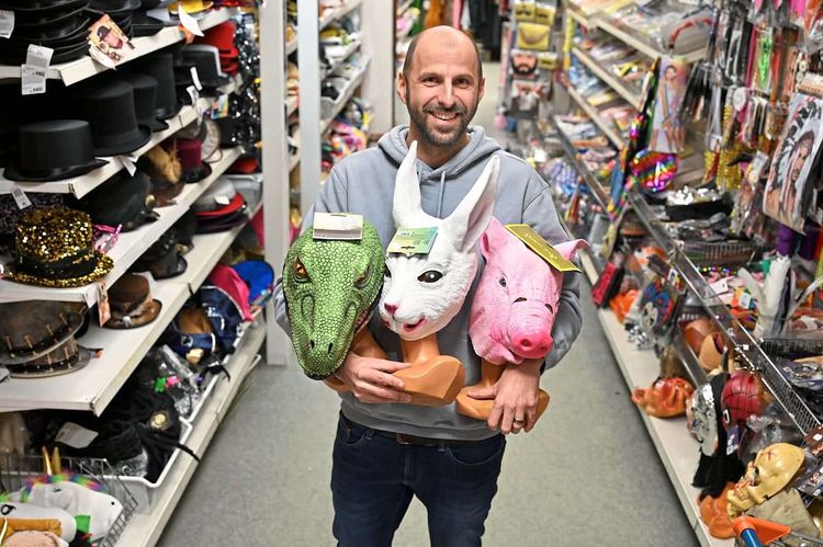 Günther Haas in seinem Geschäft, er hält Dinosaurier-, Hasen- und Schweinemasken in den Händen.