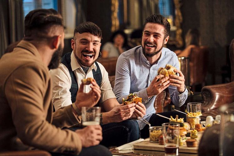 Drei junge Männer sitzen mit Burger und Pommes im Lokal