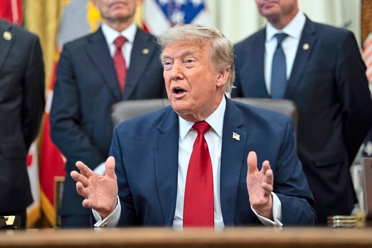 Ein Mann im Anzug und mit roter Krawatte spricht gestikulierend bei einer Zeremonie im Oval Office des Weißen Hauses. Im Hintergrund stehen mehrere Personen in formeller Kleidung.