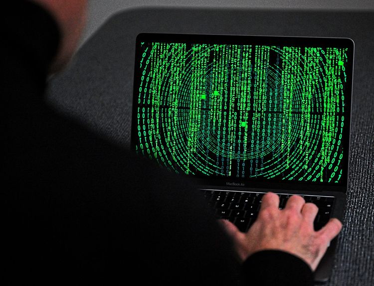Ein schwarz gekleideter Hacker vor einem Laptop mit grünen Zahlenreihen
