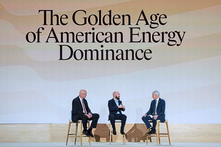 Drei Männer sitzen auf einer Bühne vor einer Leinwand mit der Aufschrift „The Golden Age of American Energy Dominance“ und diskutieren. Alle tragen Anzug, und einer spricht gestikulierend.
