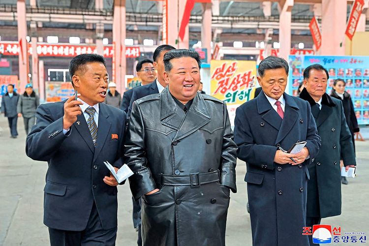 Kim Jong Un lächelt, um ihn herum stehen Männer mit Krawatte.