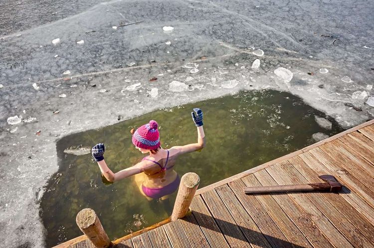 Frau badet in einem See, rund um sie eine dicke Eisschicht an der Wasseroberfläche 