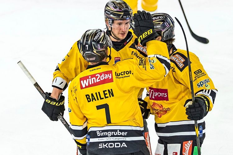 Eishockeyspieler der Vienna Capitals in gelben Trikots feiern ein Tor während eines Spiels gegen den HC TIWAG Innsbruck in der win2day ICE Hockey League. Spieler umarmen sich auf dem Eis, ein weiterer Spieler im Hintergrund trägt ebenfalls das gelbe Trikot.