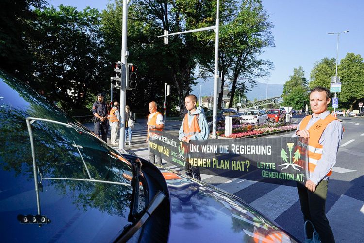 Klimaaktivisten mit Banner am Zebrastreifen, sie spiegeln sich in der Windschutzscheibe eines Autos.