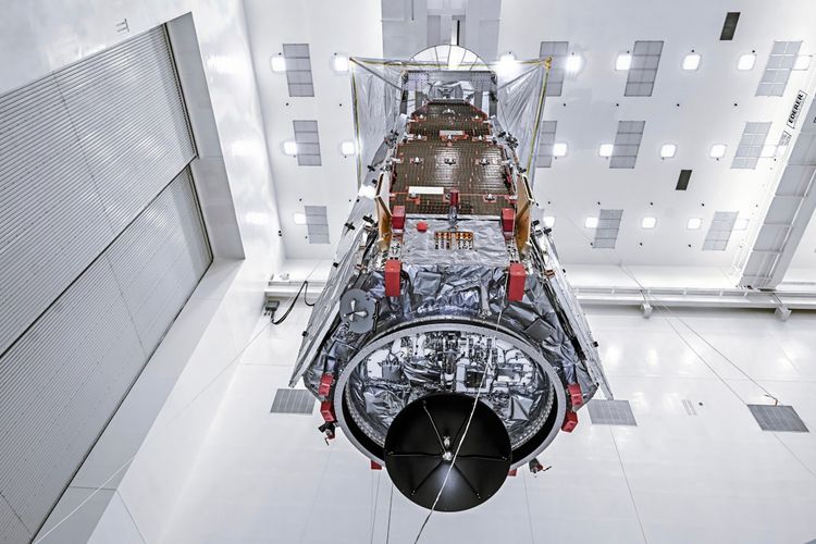 Hochauflösendes Bild des Nancy Grace Roman Space Telescope, das von Techniker:innen in einer Reinraumumgebung der NASA mit einem Kran auf einen speziellen Arbeitsstand gehoben wird. Der Satellit ist in reflektierenden Materialien verpackt und zeigt komplexe technische Strukturen.