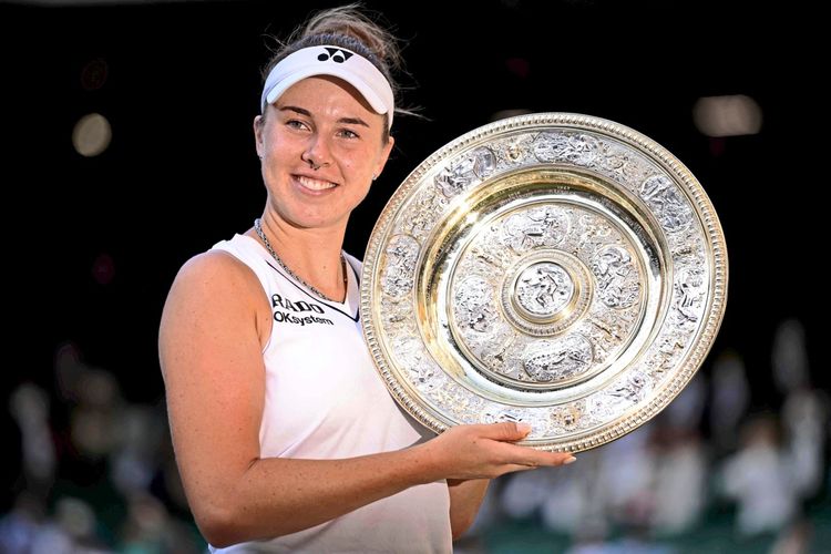 Eine Tennisspielerin in weißem Outfit hält die Venus Rosewater Dish, die Trophäe für den Sieg im Damen-Einzelfinale der Wimbledon-Meisterschaften 2026, und lächelt in die Kamera.