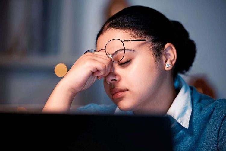 Eine Frau, die erschöpft an ihrem Computer sitzt, den Kopf in die Hand gestützt.