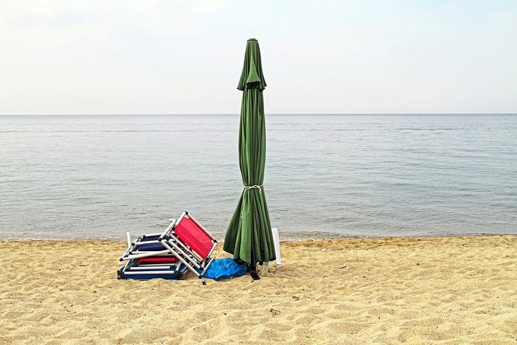 Geschlossener Sonnenschirm mit zusammengeklappten Liegen am Meer