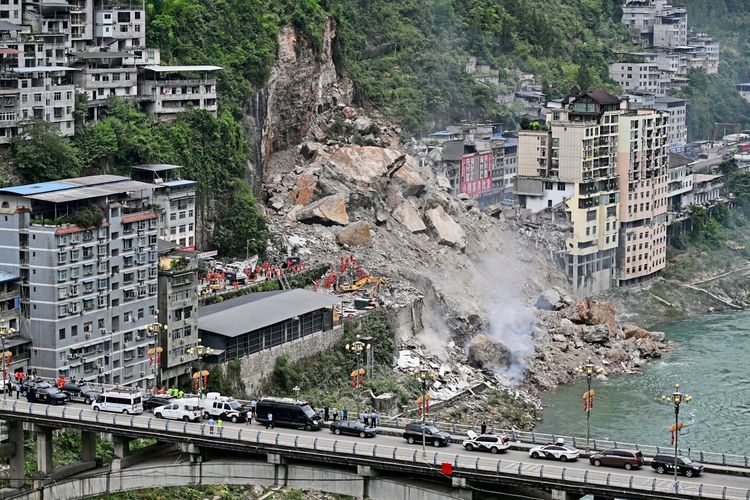Rettungskräfte suchen nach Überlebenden an der Stelle eines Erdrutsches entlang des Wujiang-Flusses in Pengshui Miao und Tujia Autonomer Kreis, Chongqing, China. Zerstörte Gebäude und Geröll sind sichtbar. Im Vordergrund verläuft eine Brücke mit Fahrzeugen.