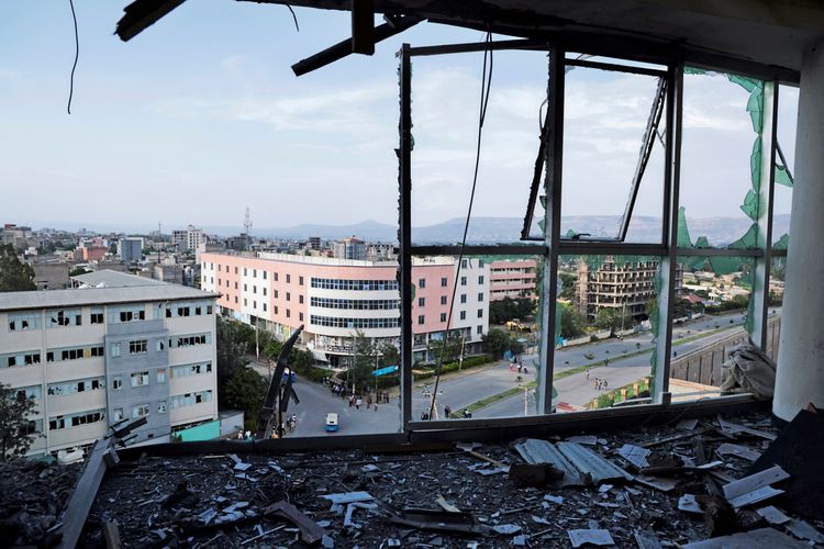 Blick durch ein zerbrochenes Fenster auf eine Stadtlandschaft in Mekelle, Äthiopien. Im Vordergrund Trümmer und Glasscherben, im Hintergrund Gebäude, Straßen und Hügel.