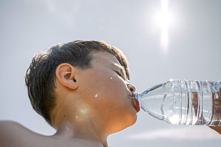 Ein Junge trinkt bei Sonnenschein aus einer Wasserflasche
