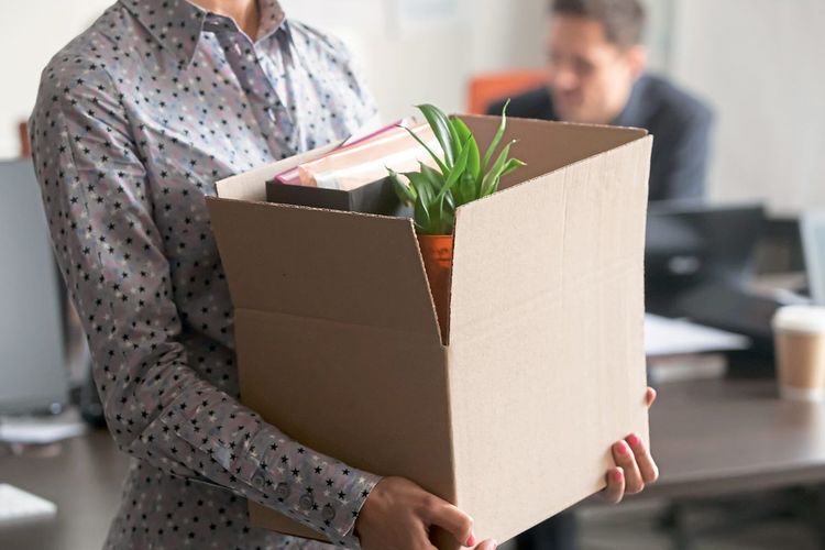 Nahaufnahme von einer Person, die mit einem gepackten Karton ein Büro verlässt