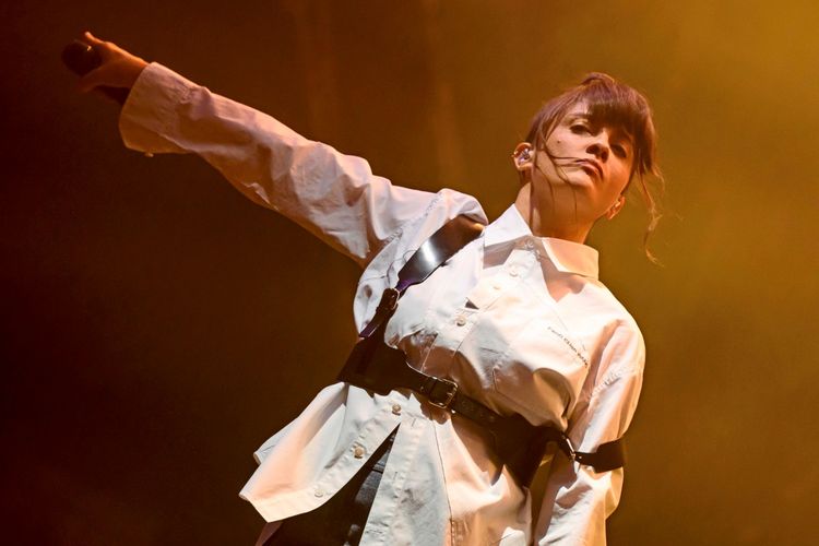 Israeli Sängerin Noga Erez tritt bei ihrem Konzert auf dem Sziget Festival auf der Shipyard Island in Budapest, Ungarn, auf. Sie trägt ein weißes Hemd und gestikuliert mit einem ausgestreckten Arm. Die Bühne ist in warmes gelb-oranges Licht getaucht.
