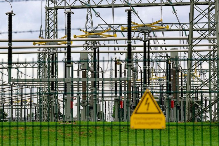 Ein Umspannwerk des Netzbetreibers Amprion, umgeben von einem massiven Zaun. Im Vordergrund ist ein Warnschild mit der Aufschrift „Hochspannung Lebensgefahr“ zu sehen. Im Hintergrund sind zahlreiche Stromleitungen und -anlagen zu erkennen. Der Himmel ist bewölkt.