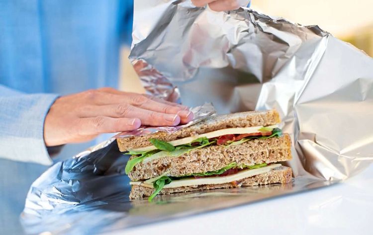 Close Up Of Woman Wrapping Sandwich In Non Reusable Aluminium Foil; Essen einpacken;
