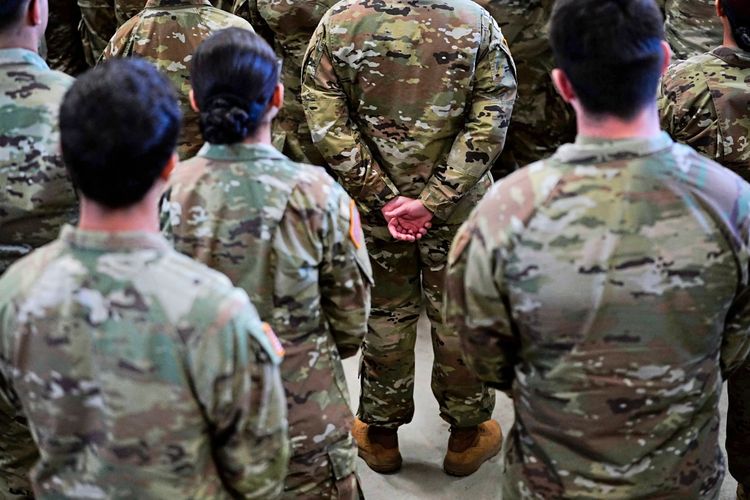 Eine Gruppe von US-Armee-Soldaten in Tarnuniformen steht mit dem Rücken zur Kamera und hört aufmerksam zu.