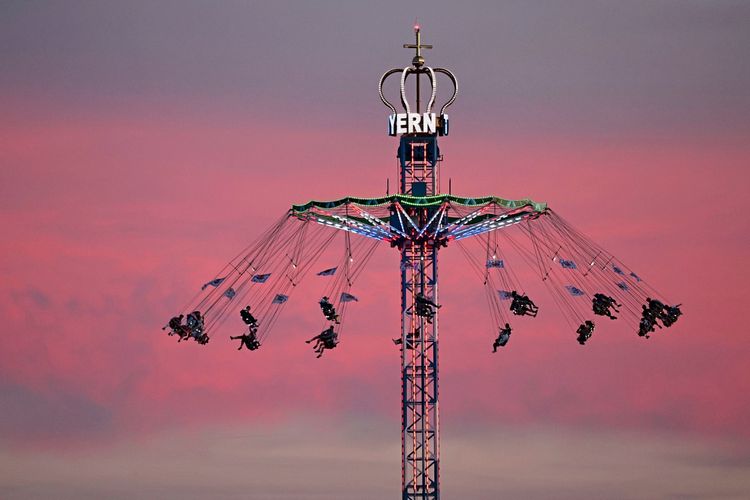 Besucher fahren auf einem beleuchteten Karussell hoch über dem Boden während eines Sonnenuntergangs am Eröffnungstag des 191. Oktoberfests in München, Deutschland.