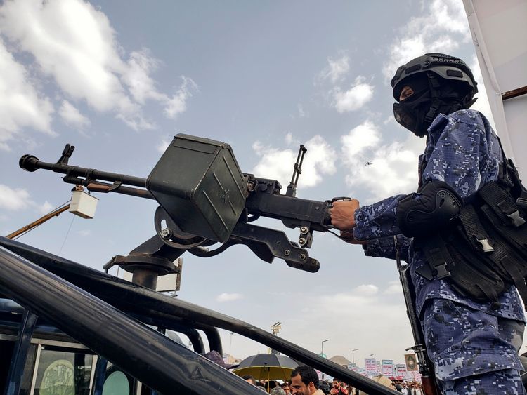 Ein Huthi-Soldat bedient ein Maschinengewehr auf einem Fahrzeug während einer Patrouille bei einer Protestveranstaltung gegen die Vereinigten Staaten in Sanaa, Jemen, am 25. April 2025. Im Hintergrund sind weitere Demonstranten und Plakate zu sehen. Der Himmel ist teilweise bewölkt.