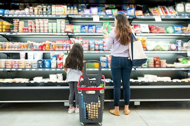 Eine Mutter mit Tochter steht vor einem Kühlregal im Supermarkt.