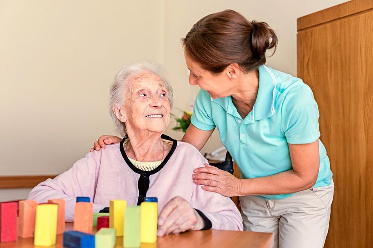 Heimpflegerin und lächelnde ältere Frau, in häuslicher Umgebung einander zugewandt