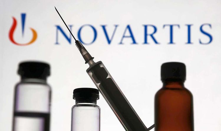 Ein Fläschchen mit Flüssigkeit und eine Spritze vor dem Logo von Novartis.