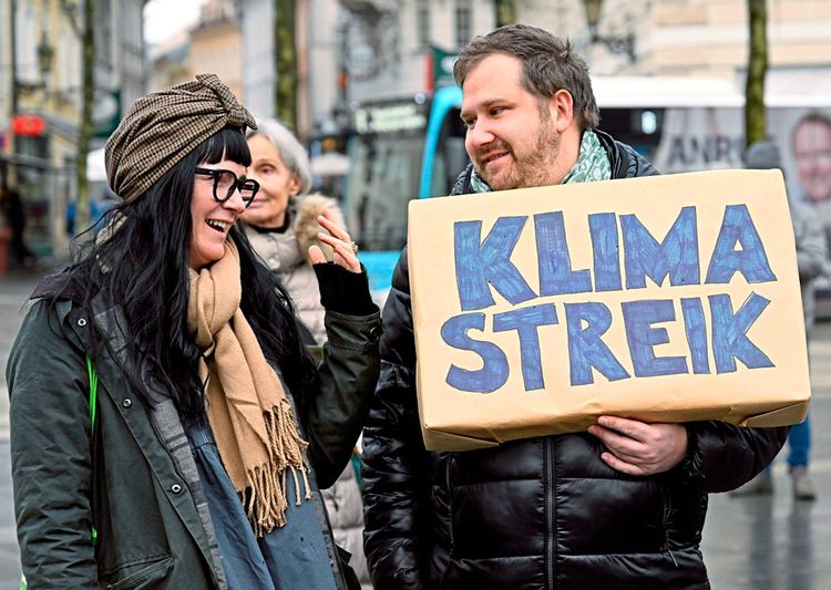 Eine junge Frau und ein junger Mann halten ein Schild im Rahmen eines Klimastreiks in die Kamera.