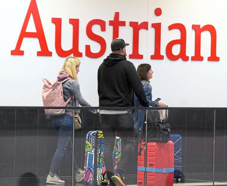 Passagiere vor einen AUA-Logo am Flughafen Wien-Schwechat.
