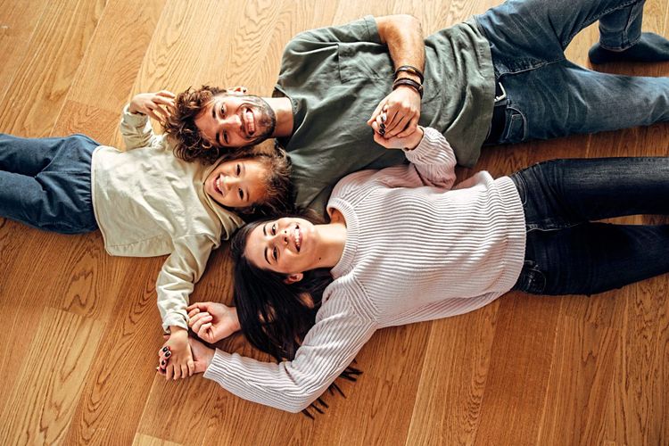 Eine Familie mit Mutter, Vater und Kind liegen auf einem Fußboden und lachen