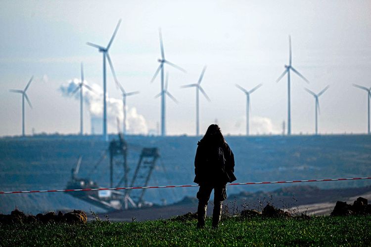 Eine Frau steht vor einem Tagebau in Deutschland, im Hintergrund drehen sich Windräder.