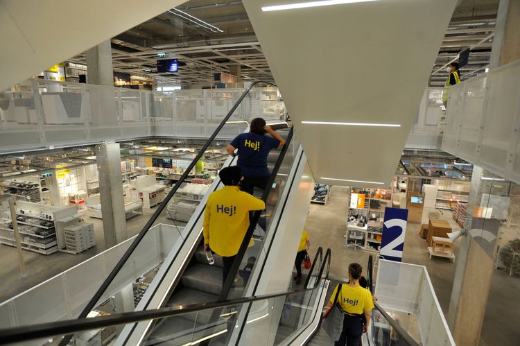 Zwei Menschen mit Ikea T-Shirts fahren eine Rolltreppe hinunter.