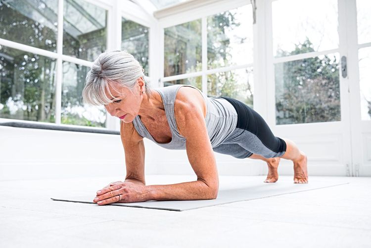Ältere Frau führt Unterarmstützt, auch Plank genannt, auf einer Sportmatte aus.