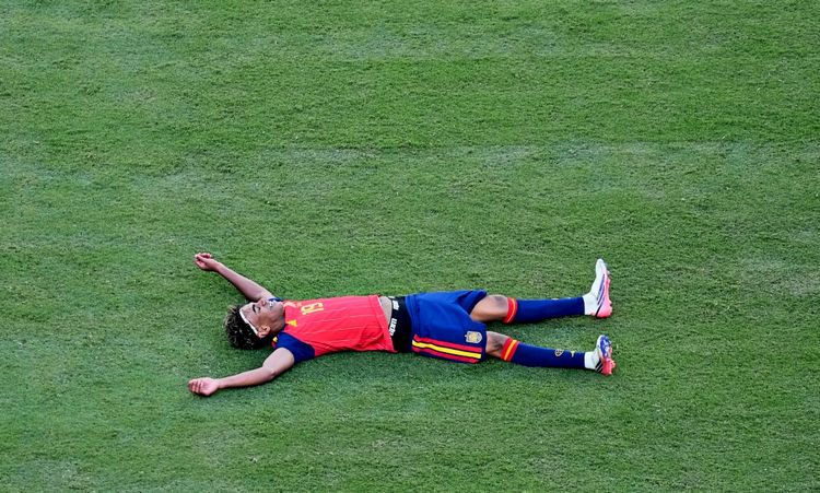 Ein Fußballspieler im Trikot der spanischen Nationalmannschaft liegt jubelnd auf dem Rasen mit ausgebreiteten Armen und Beinen.