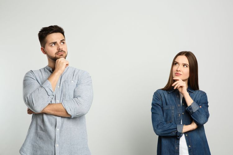 Ein Mann und eine Frau stehen vor einem weißen Hintergrund nebeneinander und blicken nachdenklich nach oben