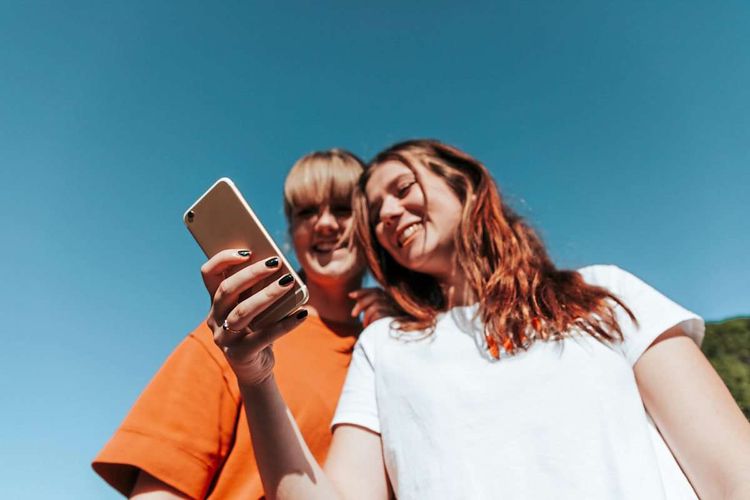 Zwei Teenagerinnen schauen gemeinsam auf ein Smartphone und lächeln
