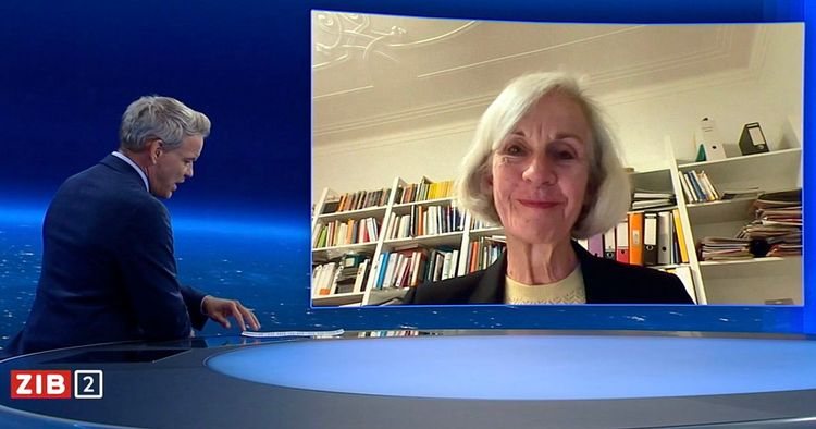 Mann mit grauen Haaren und dunklem Sakko spricht, am blauen Moderationspult der ZiB 2 sitzend, mit einer lächelnden Frau mit hellen Haaren, ins Studio zugeschaltet auf einem Display.Hinter ihr ein Bücherregal und eine weiße Stuckdecke.