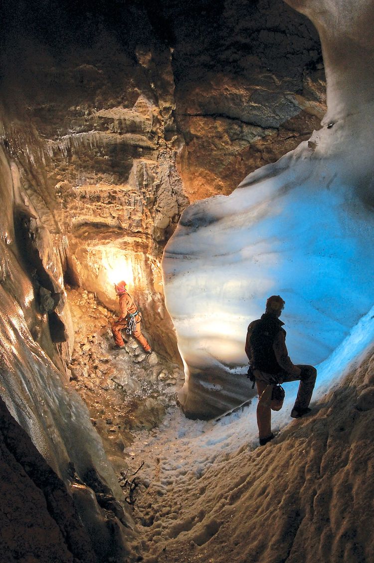 Zwei Höhlenforscher in einer Höhle mit steilen Wänden, die teilweise eingeschneit ist