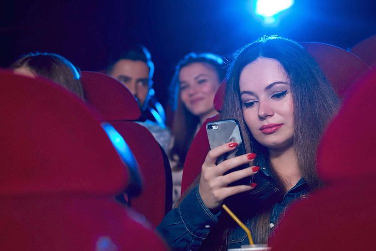 Eine Frau spielt im Kinosaal mit ihrem Handy herum