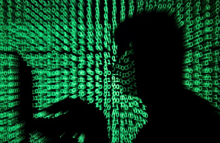 Eine Silhouette einer Person mit einem Laptop, umgeben von grünem Binärcode, der auf die Szene projiziert wird. Symbolische Darstellung von Cyberangriffen und digitaler Bedrohung.