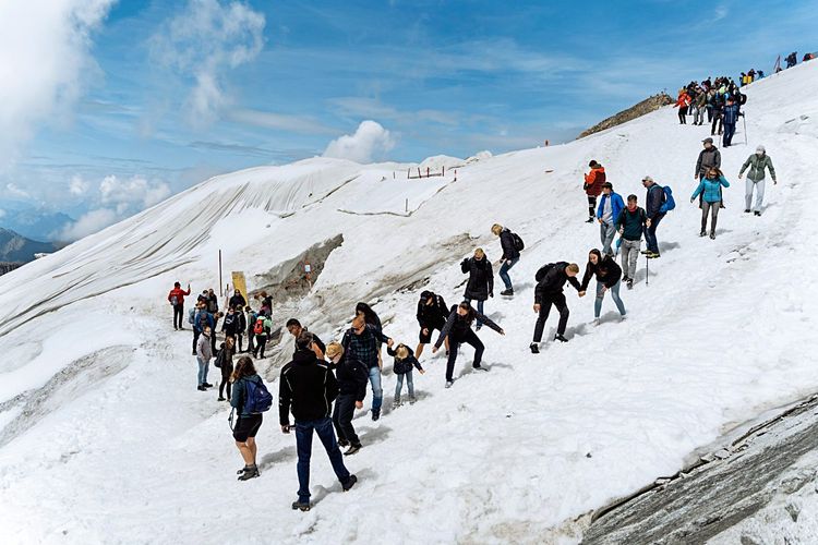 Viele Menschen rutschen über den Schnee zum Eingang einer Gletscherhöhle