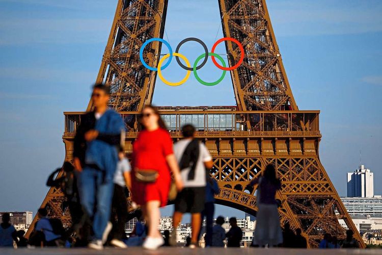 Menschen vor dem Eiffelturm, der mit olympischen Ringen geschmückt ist.