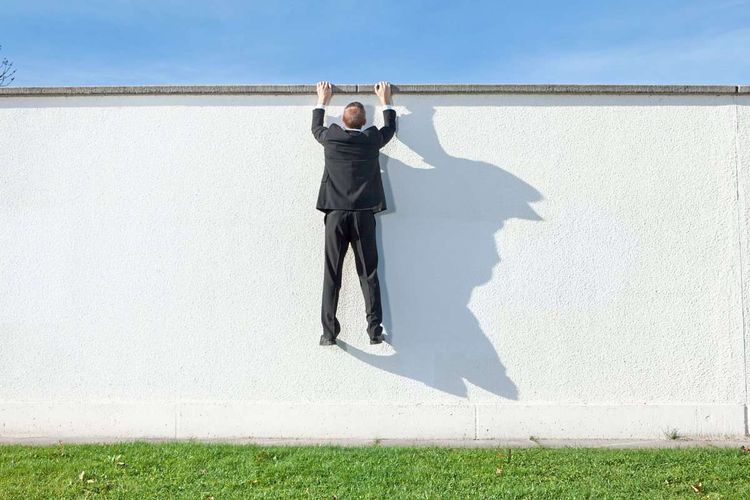 Ein Mann mit Anzug versucht über eine hohe Wand zu klettern.