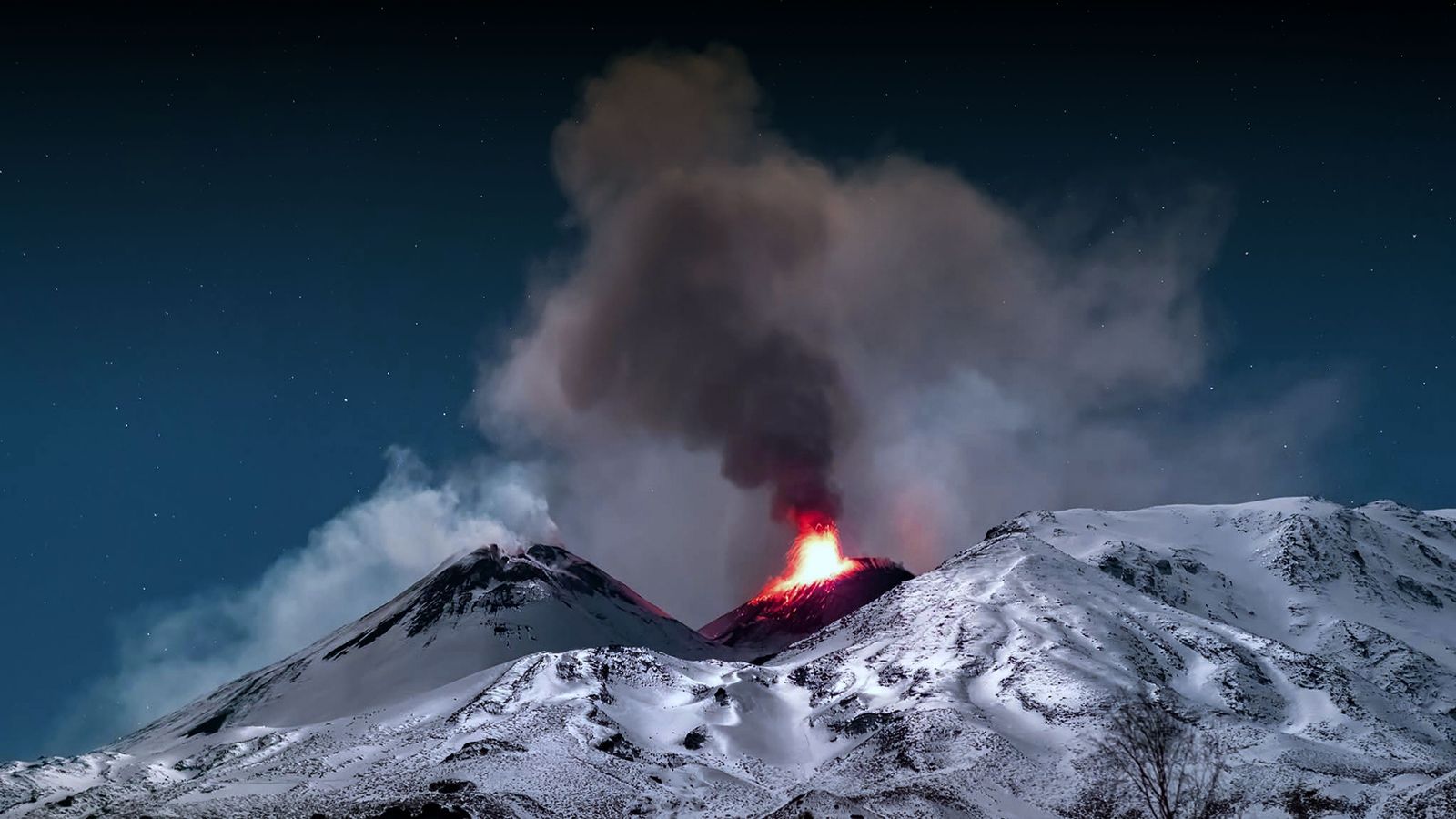 Lava bricht aus dem Schlot eines aktiven Vulkans aus. Der Berg ist mit Schnee bedeckt.