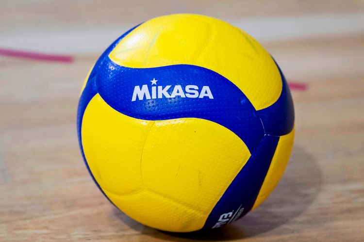 ALT-Text: Nahaufnahme eines Volleyballs der Marke Mikasa in den Farben Gelb und Blau auf einem Hallenboden.